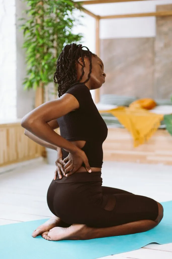 Sportswoman with dreadlocks stretching, inclining, do yoga. Female holding back, feeling pain in joints and muscles, backache. Health and body care. Side view