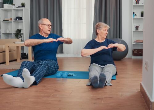 Senior couple doing seated exercises at home, stretching and engaging in light strength training with dumbbells on yoga mats.