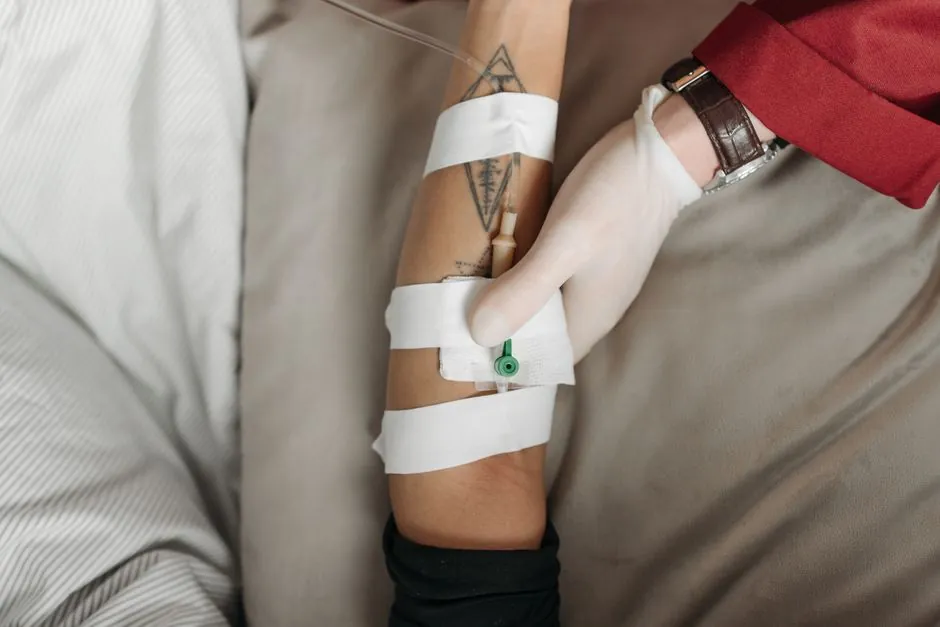 Gloved hand checking an IV cannula taped to a patient's forearm