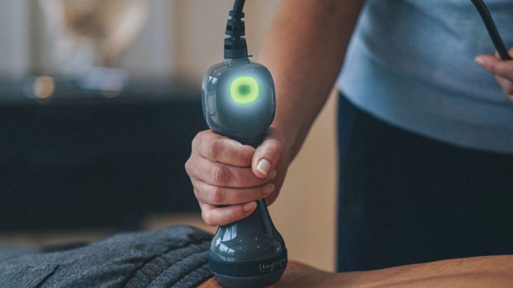 A person uses a light therapy device on another person's back.