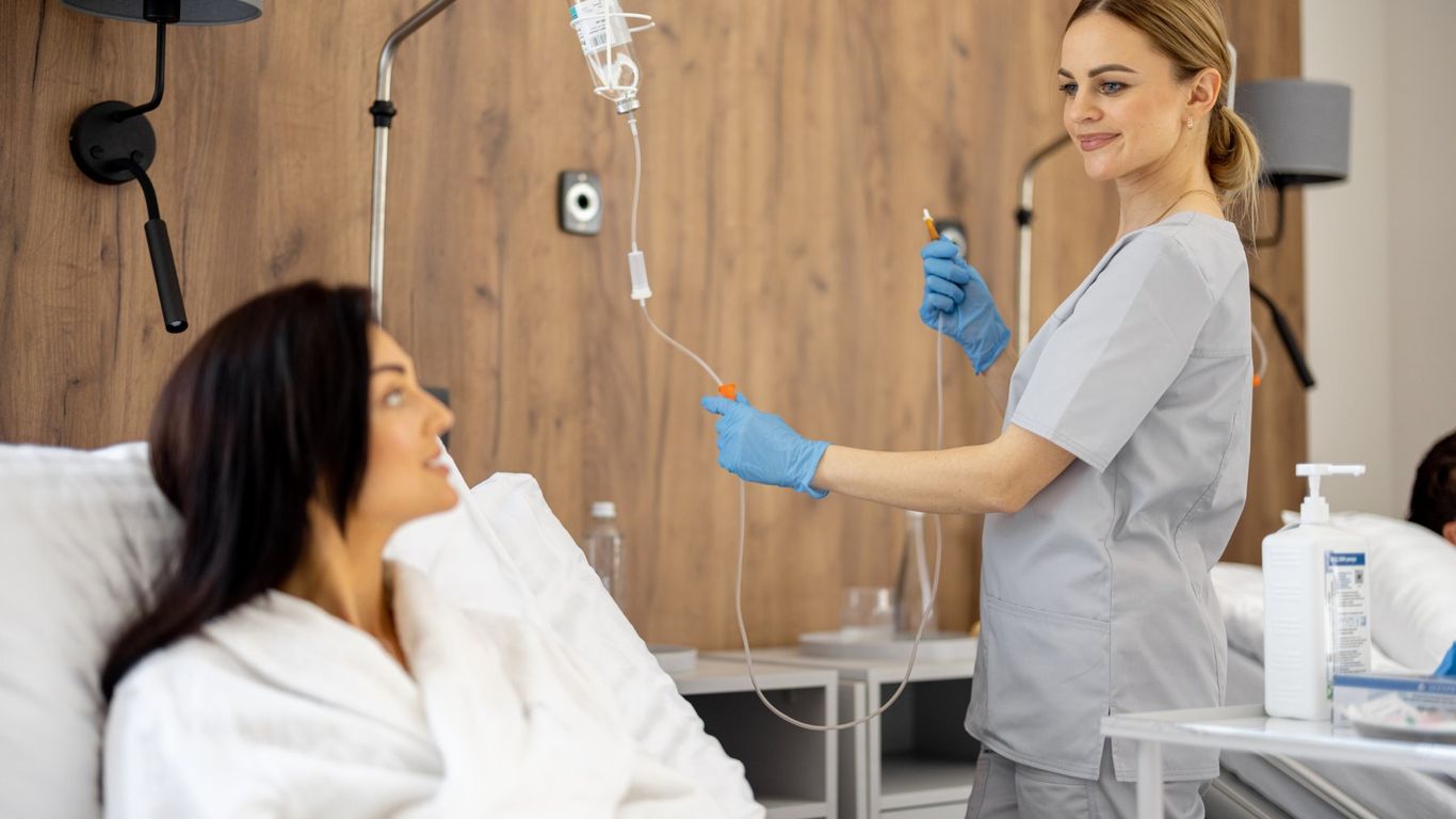 A medical professional adjusts an IV drip for a patient in a hospital room.