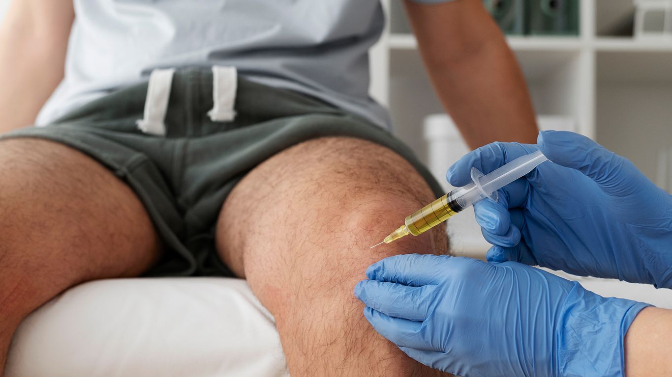 A gloved hand injects fluid into a person's knee.