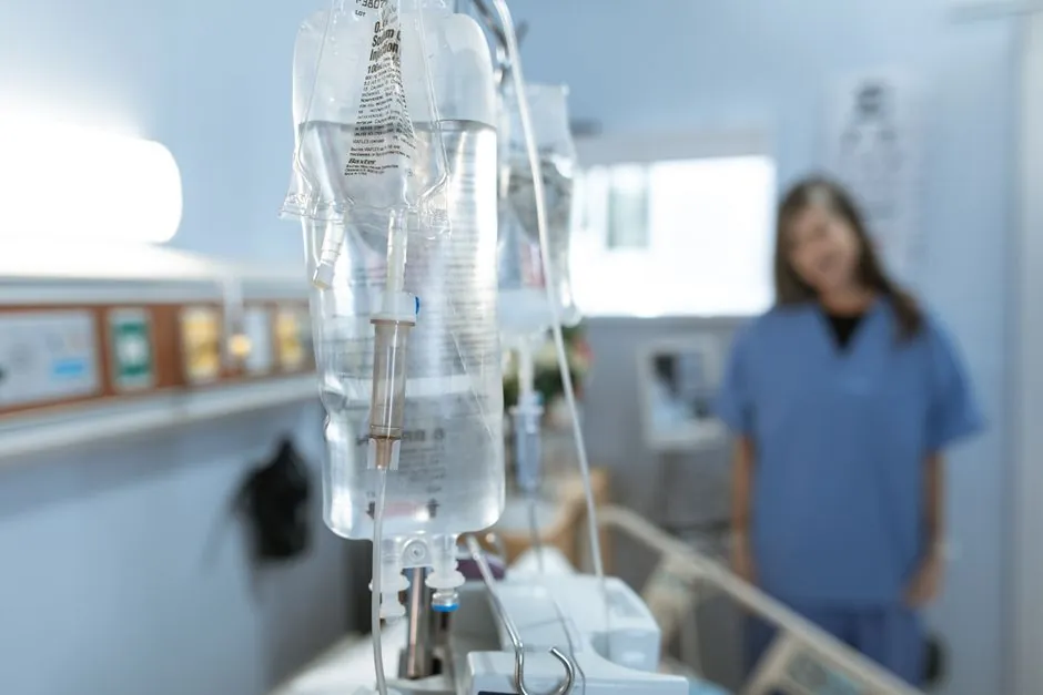 IV bags hanging in a treatment room with a nurse in the background