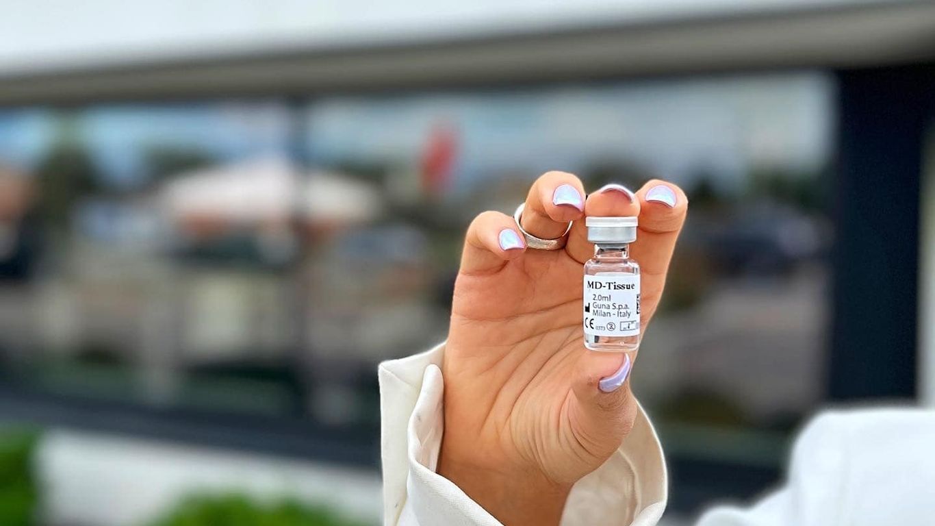 A hand holds a small vial of MD-Tissue in front of a building.