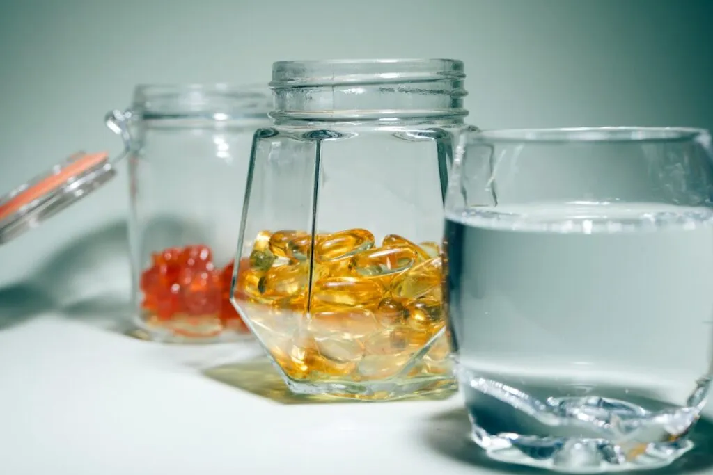 Glass jars of supplement softgels next to a glass of water