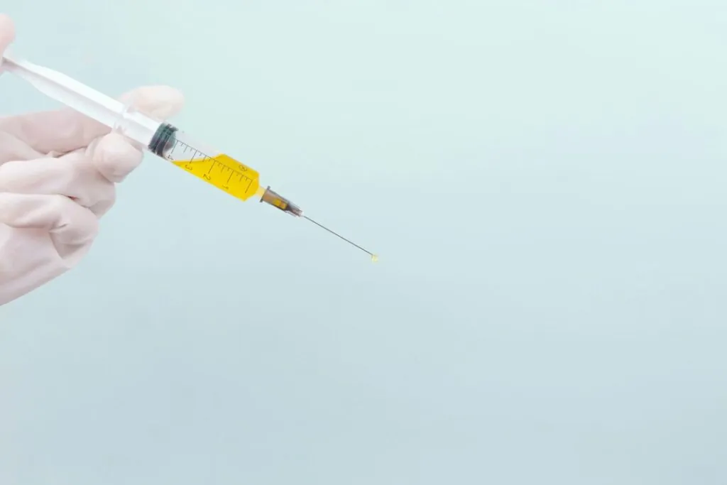 Gloved hand holding a syringe filled with yellow fluid