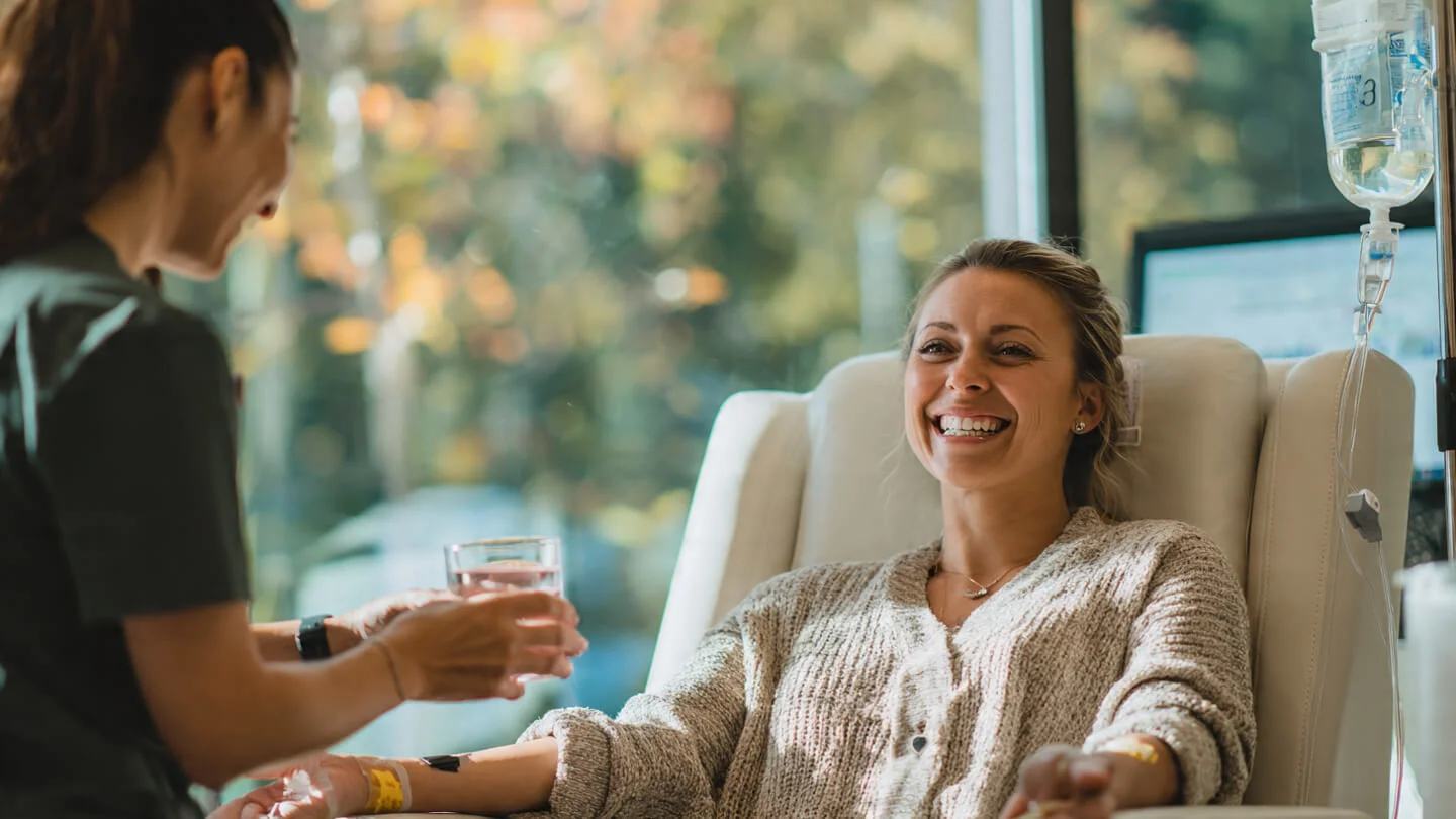 Smiling patient receiving an IV drip while a clinician offers a glass of water