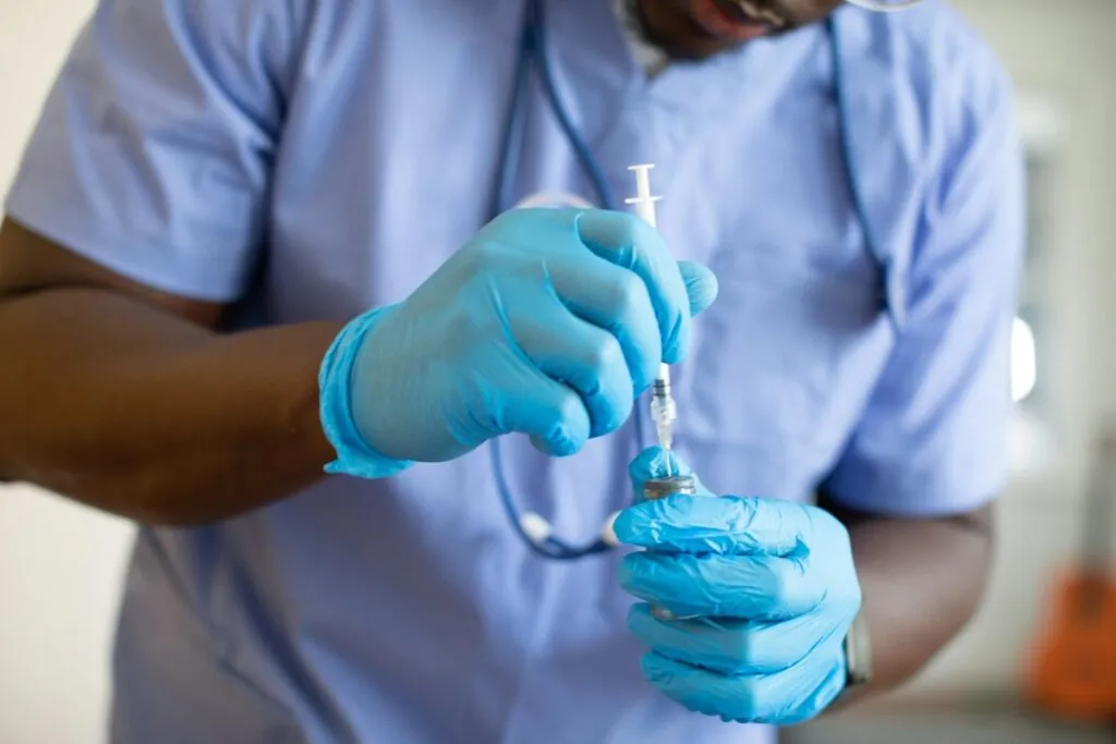 Healthcare professional in gloves drawing medication from a vial into a syringe